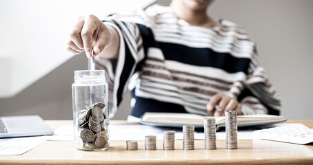 The woman was putting coins into a glass jar with lots of coins and a row of coins on the side. She is saving money every month to invest and spend it in the future. Money saving ideas.