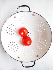 Red tomatoes in a white colander on a white background