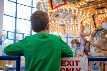 Fototapeta na wymiar Child looking at merry go round; standing in front of Exit Only sign