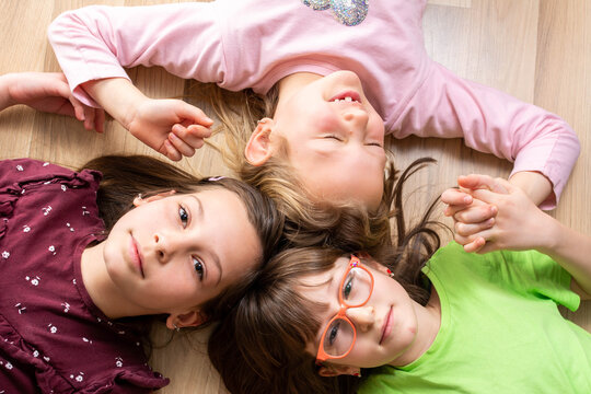 Top view of cute little girls looking at camera and smiling while lying on the floor at home. Top view creative photo of beautiful children on light wooden floor.