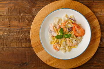 Pasta with shrimps in a creamy sauce decorated with spinach on a gray plate on a wooden table on a stand. Copy space