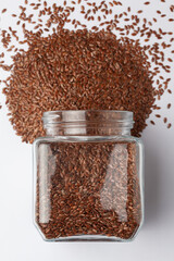 Organic Brown flaxseeds (Linum usitatissimum) or linseed, spilled and in a glass jar, Top view
