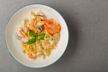 Pasta with shrimps in a creamy sauce on a gray plate on a concrete background. Copy space.