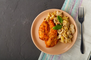 Baked chicken breast with salad on a plate decorated with spinach next to a fork on a concrete background on a gray napkin.