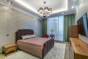 Classic interior of the bedroom. Interior design. A TV above the wooden cabinet..Daylight going through big  windows