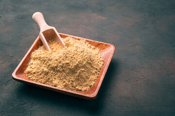 A brown wooden plate with mustard powder on a brown concrete background.