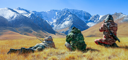 Men in camouflage with binoculars and weapons inspect the foothills.