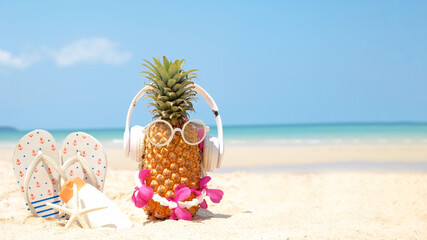 Summer party. Pineapple wearing sunglasses and listen to music with sunblock and sandal on beach and blue sky background. Tropical fashion. Summer Fashion on holiday concept.
