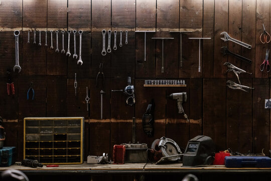 Workshop scene. Old tools hanging on wall in workshop, Tool shelf against a table and wall, vintage garage style
