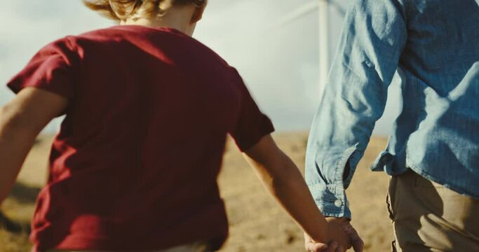 Happy father and son holding hands and walking under windmills, family lifestyle, spending quality time together, clean energy future, environment and sustainability concept