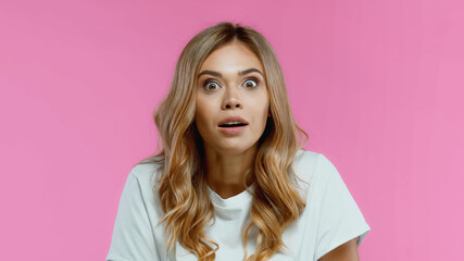 Fototapeta premium Shocked blonde woman looking at camera isolated on pink