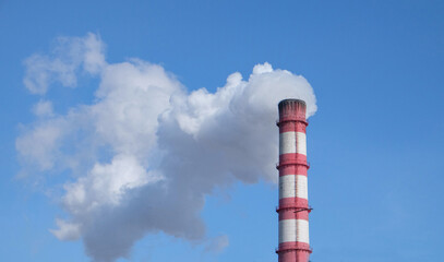 Thick white smoke from a chimney against a bright blue sky. Ecology, environmental pollution
