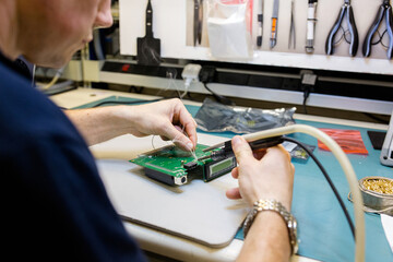 An unknown man using a soldering iron on a circuit board. Electronics, manufacturing, repairing,...