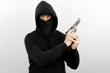Criminal man wearing balaclava and hoodie holding pistol over isolated white background. Crime...