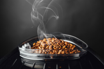 fresh roasted coffee beans with smoke in coffeemaker bean container, close-up view