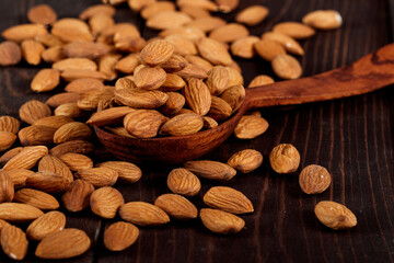 Top view of almonds on dark stone table with wood spoon or scoop. Almond in wooden bowl. Nuts freely laid on dark board.