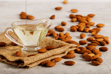 Almond oil with fresh almonds on a white wooden background. Space for text.