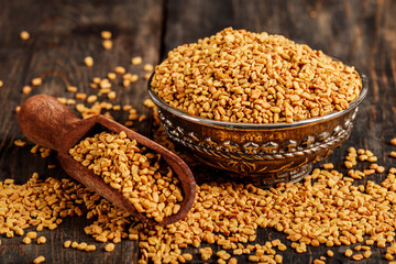 Fenugreek seeds on metal plate, spice, culinary ingredient. Fenugreek seeds in wooden spoon on textured background. Fenugreek seeds in a spoon and on a table.