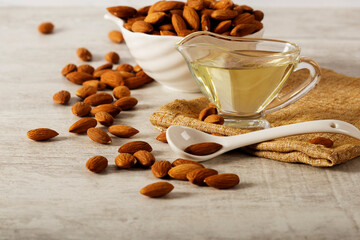 Almond oil with fresh almonds on a white wooden background. Space for text.