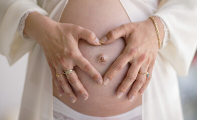 hands female embrace a pregnant belly and show the heart