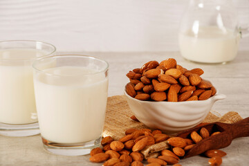 Almond milk in a glass with fresh almonds on a light wooden background.