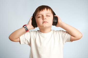 a child in headphones listens to music with his eyes closed on white background 