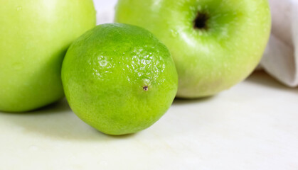 Two green apples and one whole lime on the table. The concept of a green diet.