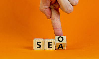 SEO vs SEA. Businessman turns a cube and changs words 'SEA - search engine advertising' to 'SEO - search engine optimization'. Business and SEO or SEA concept. Beautiful orange background, copy space.