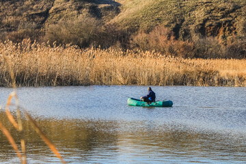 A man in an old inflatable boat is fishing in the lake with a fishing rod, but against the background of yellow reeds