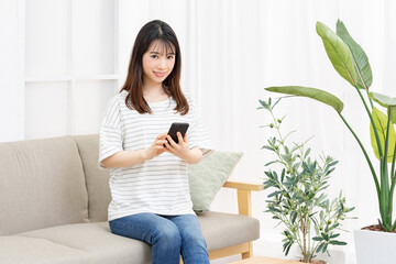 部屋のソファーに座ってスマホを操作する若い女性