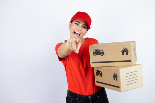 Young beautiful woman wearing courier uniform holding delivery packages laughing at you, pointing finger to the camera with hand over body, shame expression