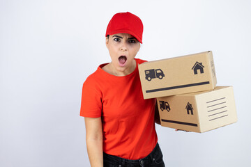 Young beautiful woman wearing courier uniform holding delivery packages afraid and shocked with surprise and amazed expression, fear and excited face.