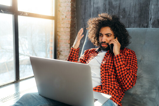 Handsome Young Egyptian Man Sitting On The Couch Working At The Computer And Talking On The Phone