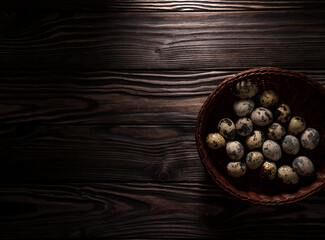 Obraz na płótnie Canvas Collected quail eggs in a wicker basket. Wooden dark background. Top view