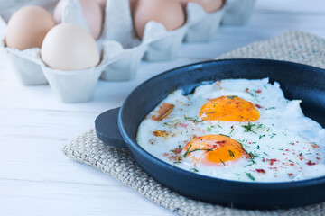 Scrambled eggs in a black cast iron pan and eggs in a tray. Light protein breakfast.