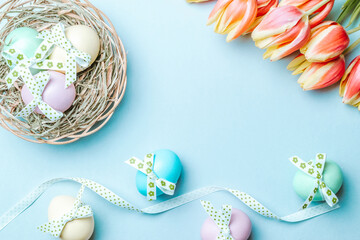 Easter card. Colourful egg with tape ribbon, spring tulips, feathers on pastel blue background in Happy Easter decoration. Flat lay, top view with copy space.
