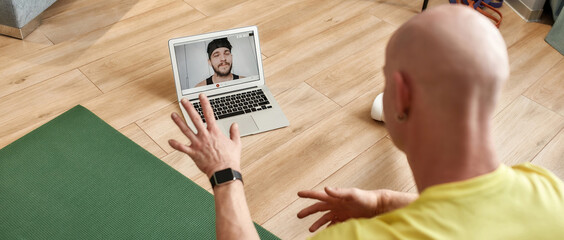 Rear view of a male fitness instructor explaining workout technics online, having video conference,...