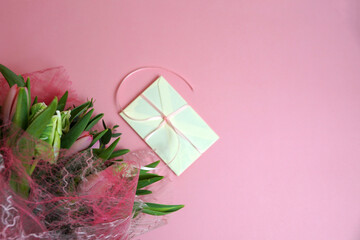 a bouquet of tulips and a gift envelope on a pink background copy space
