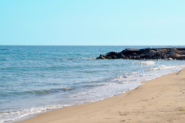 Fototapeta na wymiar empty sandy beach, big stones on the shore, sea horizon and clear sky