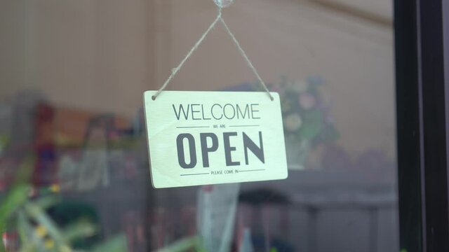 Asian woman wear mask turning Welcome we are open sign on fronton glass door cafe. Asian woman wear mask turning Welcome we are open sign on fronton glass door cafe. Restarting again and keep forward 