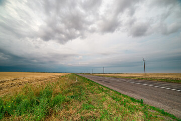 Fototapeta na wymiar an asphalt road among the fields over which thunderclouds hang
