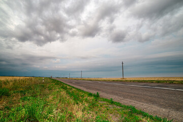 Fototapeta na wymiar an asphalt road among the fields over which thunderclouds hang