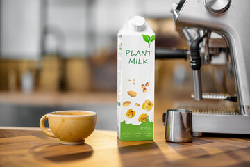 Packaging of vegetable milk near a cup of coffee, pincher and coffee machine on wooden table top on the kitchen. Organic nut dairy, alternative drink. Copy space.