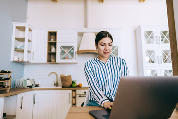 Young caucasian woman using laptop computer, sitting on the kitchen at home.