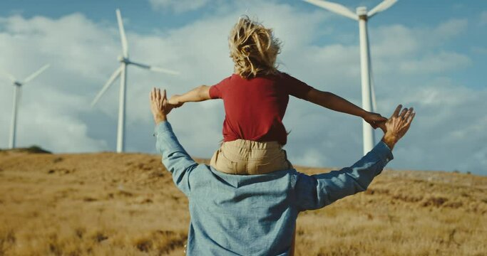 Father with young son on his back looking out at windmills on the hillside, cleaner and sustainable future, climate change, father and son bonding