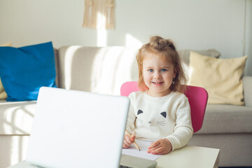 A little girl of 3 years old is studying online. The little girl draws. Quarantine.