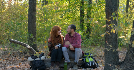 young couple of travelers with binoculars and photo camera walk in autumn forest	