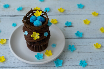 Chocolate easter cupcake with chocolate nest and decorative eggs. Spring flowers. Rustic wood background