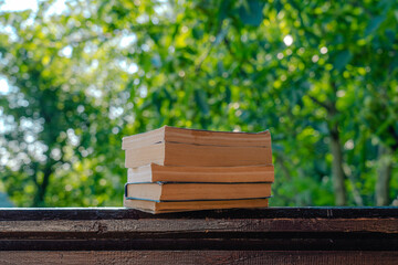 Fototapeta premium Closeup view photography of several vintage paper books laying on organic wooden background isolated on green blurry natural bokeh background
