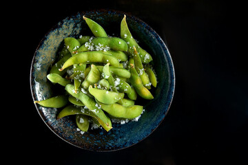 Edamame bean salad with sea salt served in a dark bowl. Isolated on a black background. Restaurant food. Japanese kitchen